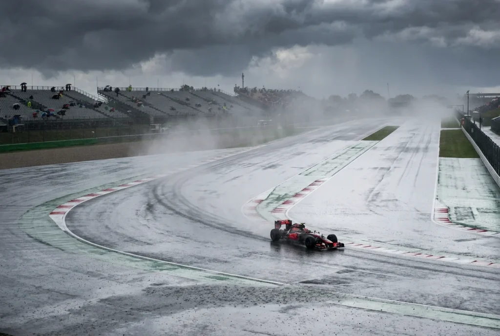 Circuito de Formula 1 bajo cielo nublado con lluvia cayendo sobre el asfalto mojado y un monoplaza rodando en pista humeda